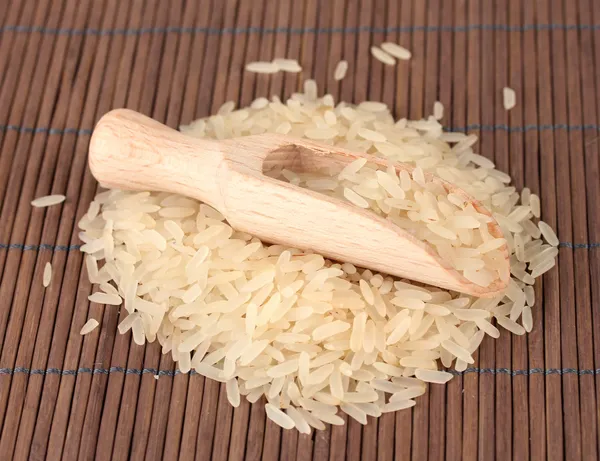 Rice in wooden scoop on bamboo mat — Stock Photo, Image