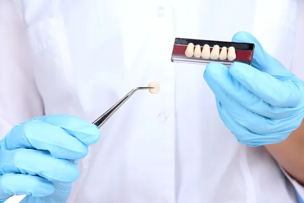 Зубной пинцет и зубной протез в руках стоматолога — стоковое фото