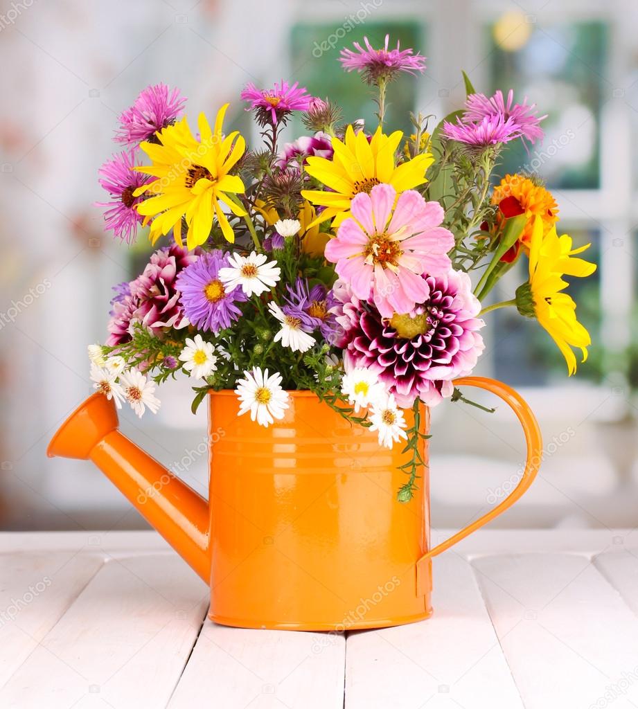 Beautiful bouquet of bright flowers in watering can on wooden table ...