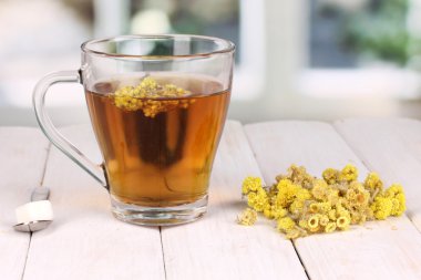 A cup of tea with immortelle on wooden table on window background clipart