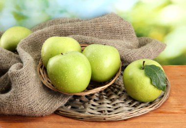 Olgun yeşil elma sepeti üzerine çuval bezi, yeşil zemin üzerine ahşap tablo