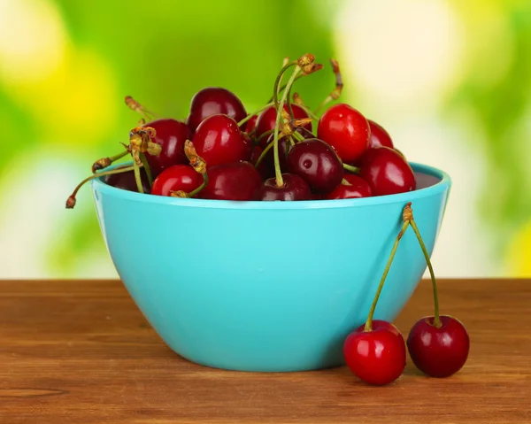 Cherry in blue bowl on wooden table on green background — Stock Photo, Image