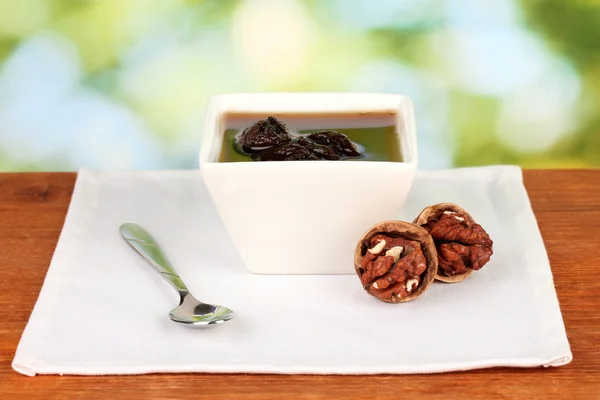 Marmelade, Walnüsse in einer Schüssel auf einem Tisch vor grünem Hintergrund — Stockfoto