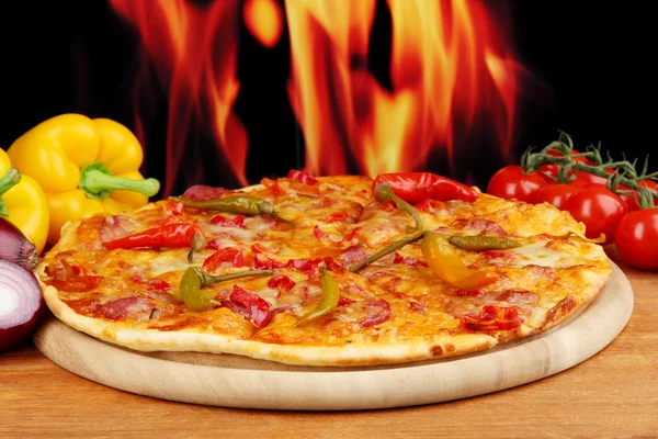 Tasty pepperoni pizza with vegetables on wooden board on flame background — Stock Photo, Image