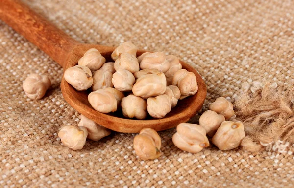 White chickpeas over wooden spoon on sackcloth background