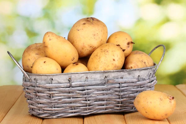 Reife Kartoffeln auf Korb auf Holztisch vor natürlichem Hintergrund — Stockfoto