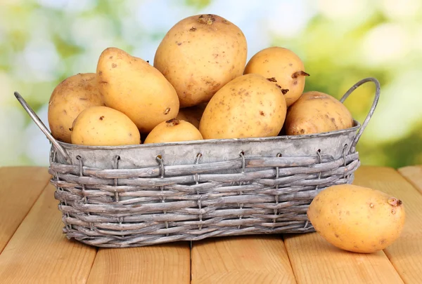 Ripe potatoes on basket on wooden table on natural background — Stock Photo, Image