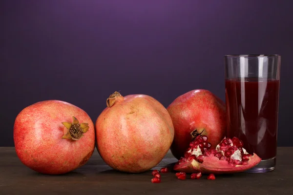 Ripe pomegranates with glass of pomegranate juice on purple background — Stock Photo, Image