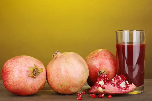 Ripe pomegranates with glass of pomegranate juice on yellow background — Stock Photo, Image