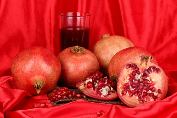 Granadas maduras con vaso de jugo de granada sobre fondo de tela roja — Foto de Stock