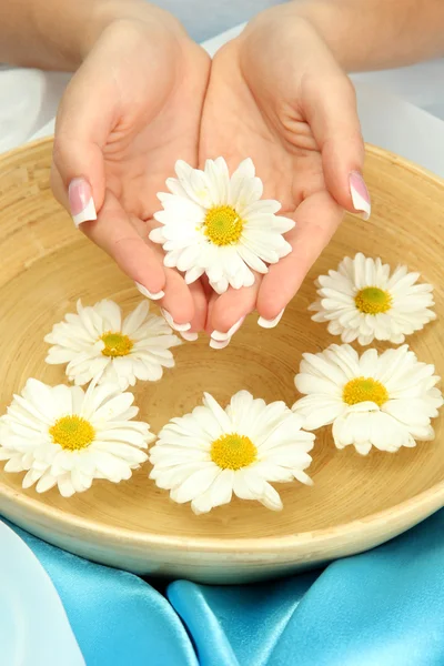 Woman hands with wooden bowl of water with flowers, on blue background — Stock Photo, Image