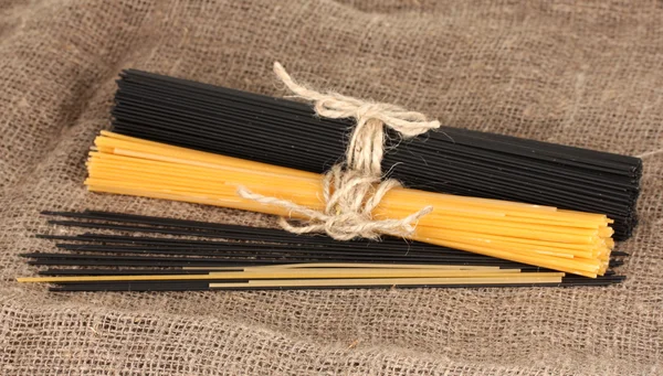 Black and yellow spaghetti on sackcloth background — Stock Photo, Image