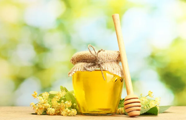 Burk med linden honung och blommor på träbord på grön bakgrund — Stockfoto