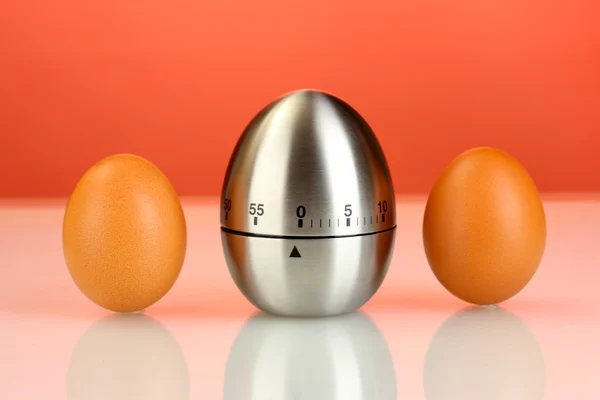 Egg timer and eggs on red background — Stock Photo, Image