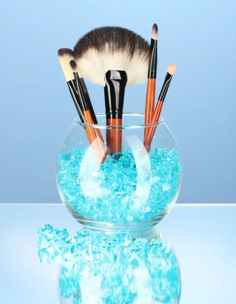 Make-up brushes in a bowl with stones on blue background — Stock Photo, Image