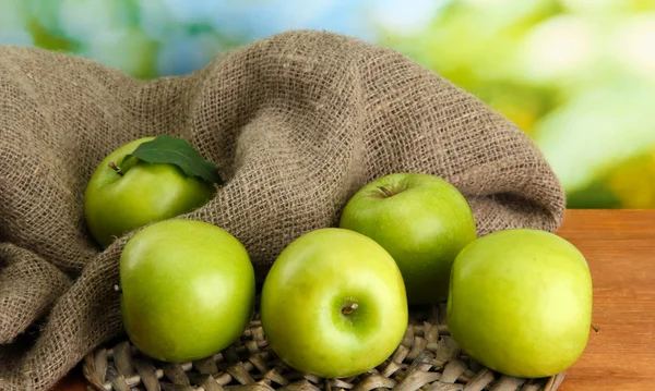 Reife grüne Äpfel mit Blättern auf Klette, auf Holztisch, auf grünem Hintergrund — Stockfoto