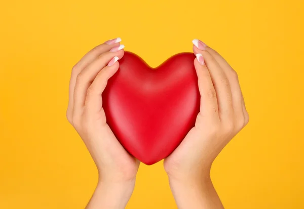 Rood hart in handen van de vrouw, op oranje achtergrond close-up — Stockfoto