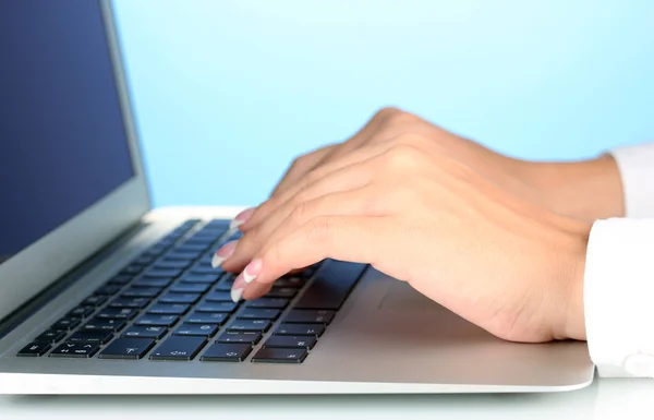 Manos escribiendo en el teclado del ordenador portátil de cerca sobre fondo azul —  Fotos de Stock