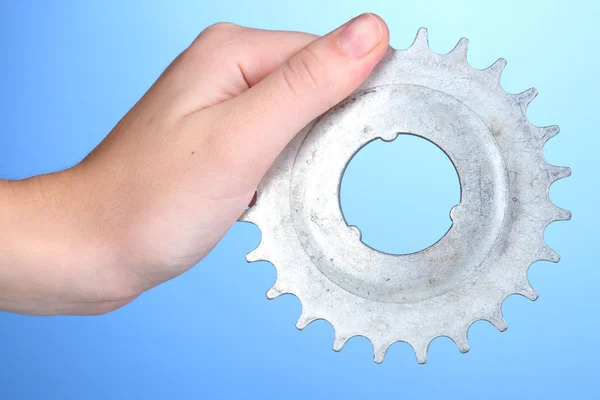 Man holding metallic cogwheel in his hand on blue background — Stock Photo, Image