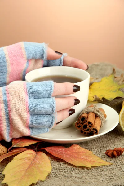 Manos sosteniendo taza de bebida caliente y hojas de otoño, sobre fondo de arpillera — Foto de Stock