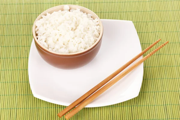 Tigela de arroz e pauzinhos na placa no tapete de bambu — Fotografia de Stock