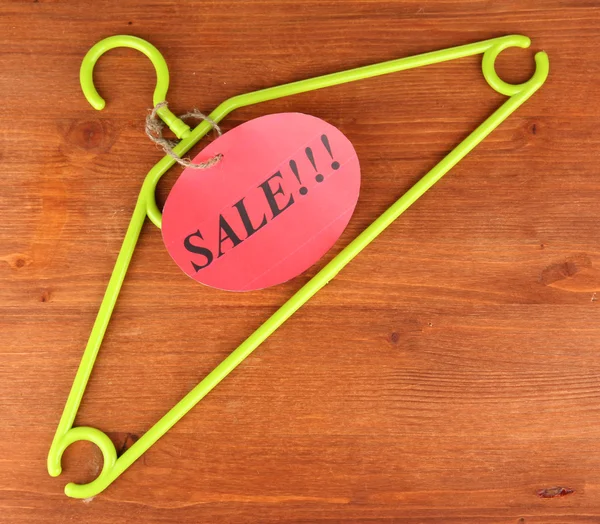 Coat hanger with sale tag on wooden background — Stock Photo, Image