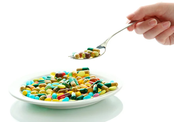 Colorful capsules and pills on plate with spoon in hand, close up — Stock Photo, Image