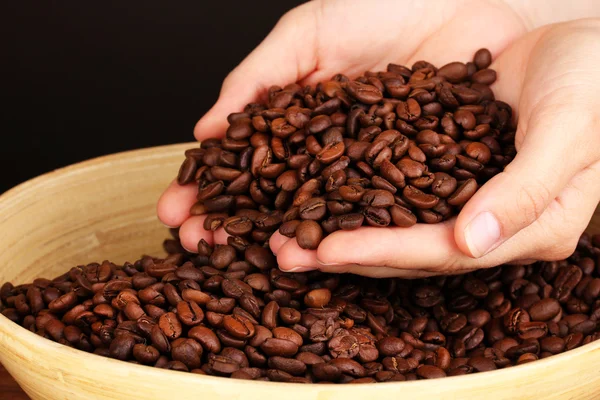 Grãos de café nas mãos sobre fundo escuro — Fotografia de Stock