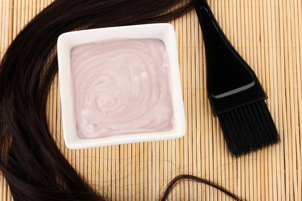 Tintura per capelli in ciotola e pennello per la colorazione dei capelli su tappetino di bambù beige, primo piano — Foto Stock