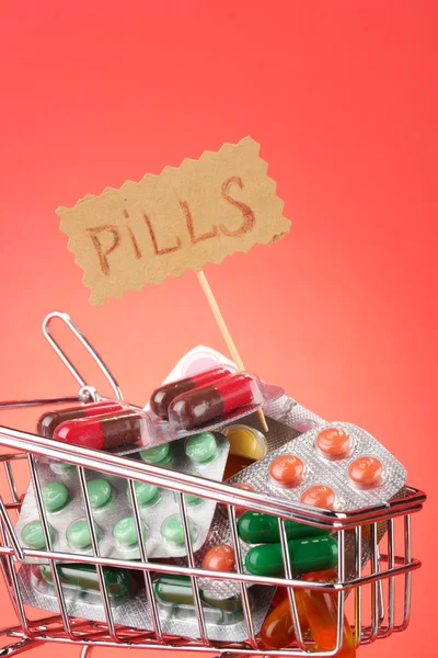 Carrello della spesa con pillole, su sfondo rosso — Foto Stock