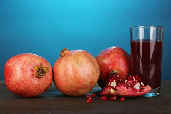 Ripe pomegranates with glass of pomegranate juice on blue background — Stock Photo, Image