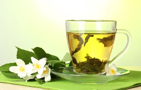 Tasse de thé vert avec des fleurs de jasmin sur table en bois sur fond vert — Photo