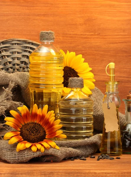 Oil in bottles, sunflowers and seeds, on wooden background — Stock Photo, Image