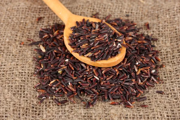 Black rice on sacking in wooden spoon — Stock Photo, Image