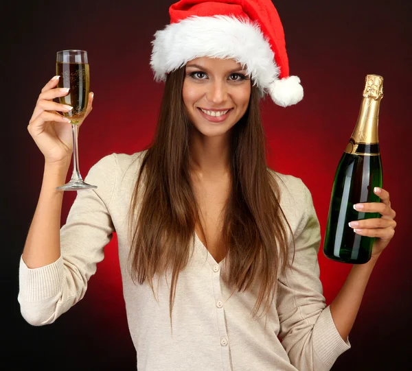 Beautiful young woman with bottle and glass of champagne, on red background — Stock Photo, Image