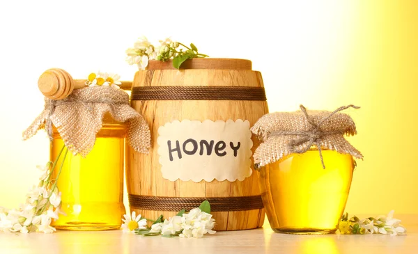 Sweet honey in barrel and jars with acacia flowers on wooden table on yello — Stock Photo, Image