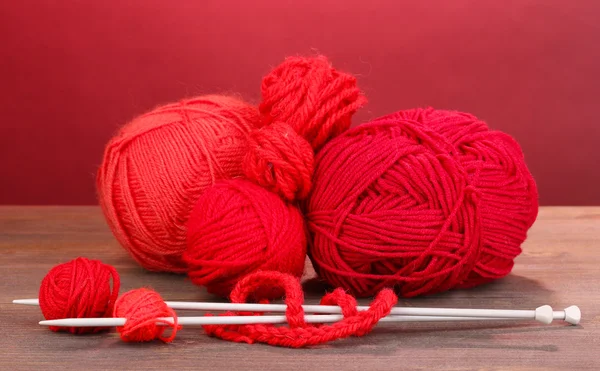Red knittings yarns on wooden table on red background — Stock Photo, Image