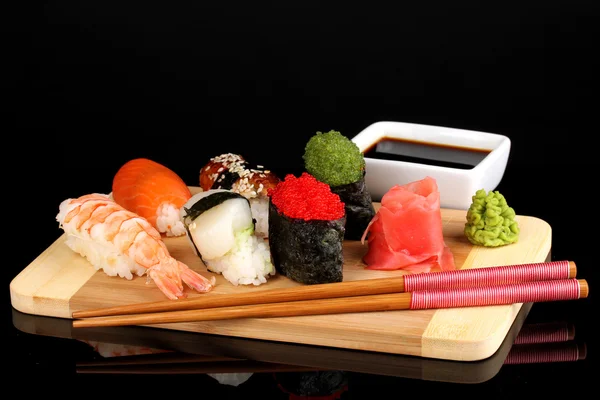 Lahodné sushi podávané na dřevěném prkénku izolovaných na černém — Stock fotografie