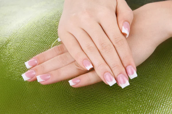 Mãos de mulher com manicure francês e flores no fundo verde — Fotografia de Stock