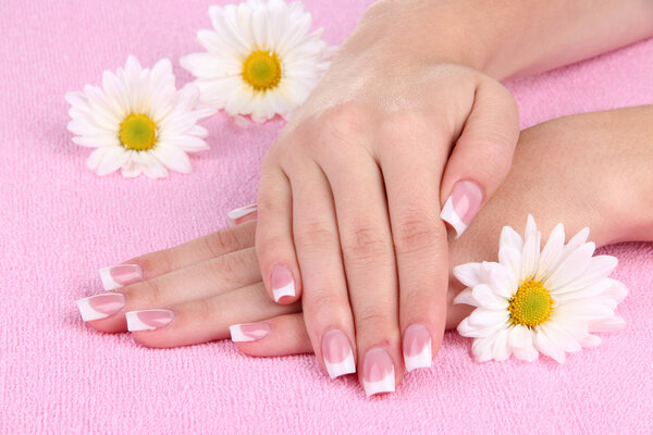 Woman hands with french manicure and flowers on pink towel