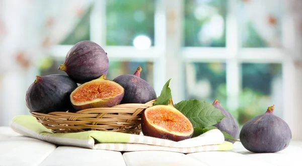 Ripe sweet figs with leaves in basket, on wooden table, on window backgroun — Zdjęcie stockowe