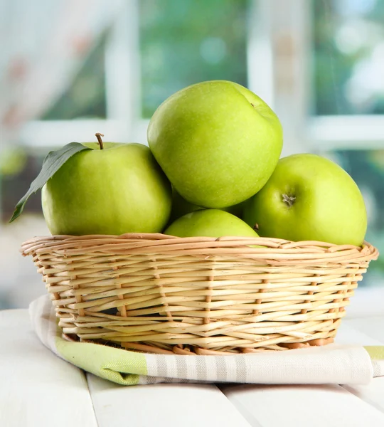 Ripe green apples with leaves in basket, on wooden table, on window backgro — Stock Photo, Image
