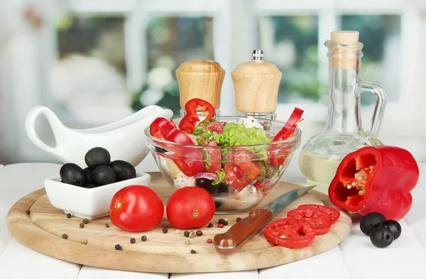 Fresh greek salad in glass bowl surrounded by ingredients for cooking on wo