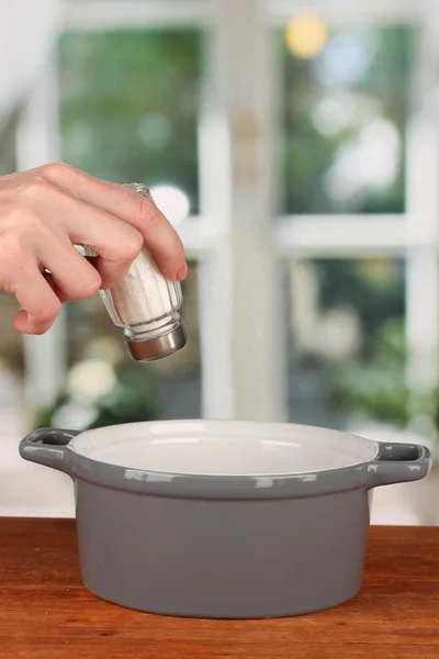 Hand adding salt using salt shaker on bright background — Stock Photo, Image