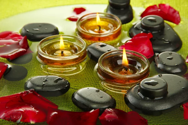 Spa stones with rose petals and candles in water on plate Royalty Free Stock Photos