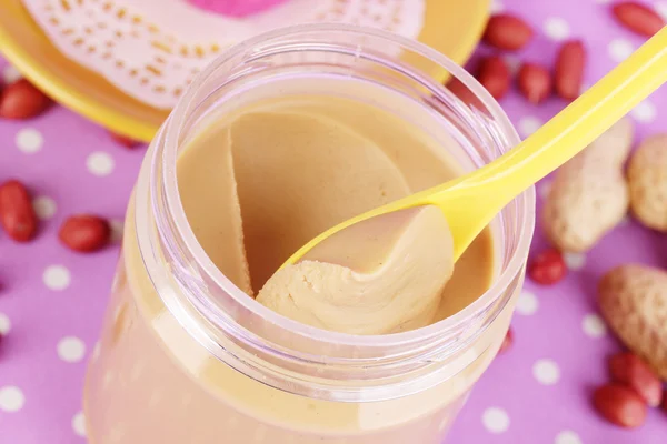 Köstliche Erdnussbutter in offener Bank auf lila Hintergrund mit Tupfen c — Stockfoto