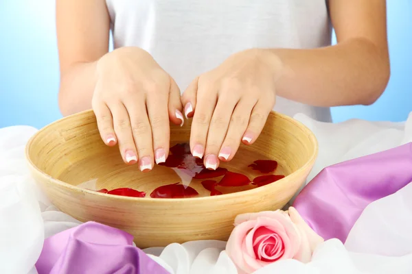 Mani di donna con ciotola di legno di acqua con petali, su sfondo blu — Foto Stock