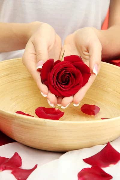 Woman hands with wooden bowl of water with petals, on red background — Stock Photo, Image