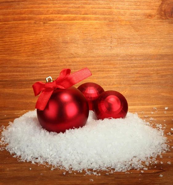 Красивые красные рождественские шары на снегу, на деревянном фоне — стоковое фото