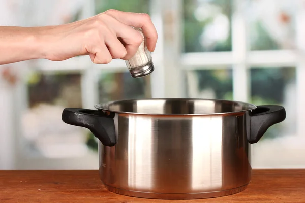 Hand adding salt using salt shaker on bright background — Stock Photo, Image